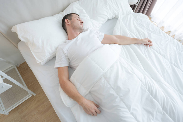若い男は快適な白い寝室で眠っていた体に休息を与える. - 写真・画像