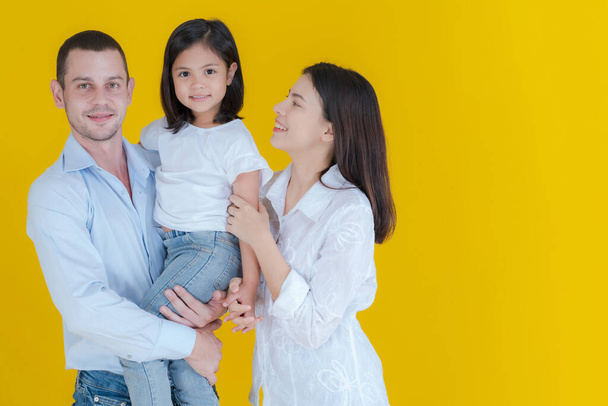 Семейный портрет отец стоит держа свою милую дочь и улыбающаяся мать стоит рядом Дети обнимают счастливых родителей, чтобы провести время вместе с семьей на желтом фоне. - Фото, изображение