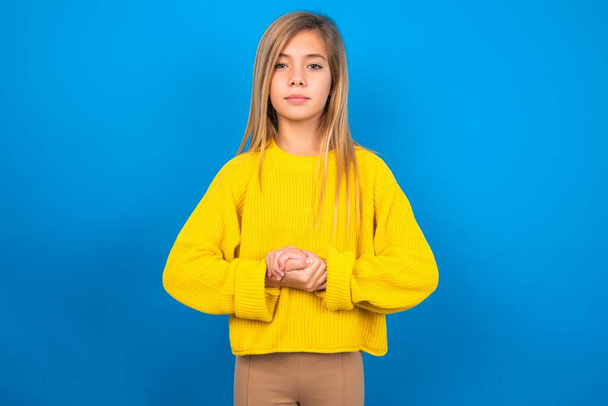 Fotografie veselý sebevědomý kavkazský dospívající dívka na sobě žlutý svetr přes modré studio pozadí  - Fotografie, Obrázek