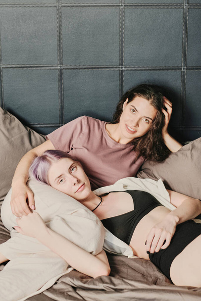 Content attractive Caucasian lesbian in black underwear lying on knees of girlfriend in bedroom - Foto, imagen
