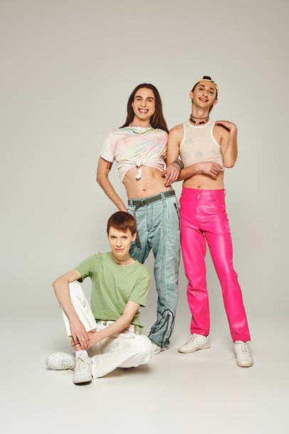 Diverse group of happy young lgbt community friends in colorful clothes smiling while celebrating pride month together and looking at camera on grey background in studio  - Foto, Imagem