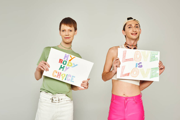 happy gay men holding placards with my body my choice and love is love lettering while standing together and looking at camera on pride month, grey background  - Foto, Imagen