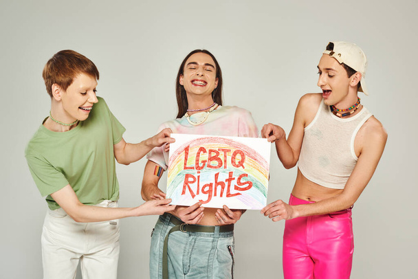 boldog lgbt barátok színes ruhák gazdaság placard lgbtq jogok betűkkel, miközben áll együtt, és mosolyog a büszkeség hónap, szürke háttér  - Fotó, kép