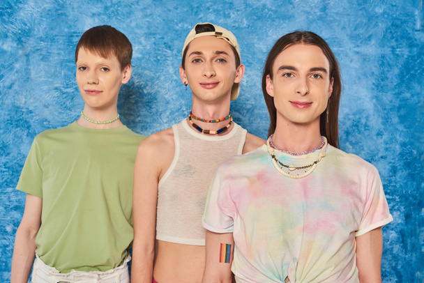 Portrait of young and stylish homosexual community looking at camera during lgbt pride month celebration on mottled and textured blue background - Zdjęcie, obraz