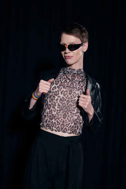 Fashionable homosexual man in blouse with animal print and sunglasses posing during lgbt community month party isolated on black  - Foto, immagini