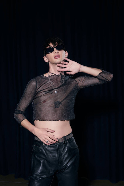 Fashionable homosexual man in sunglasses, sparkling top and necklaces posing during lgbt community month party isolated on black  - Фото, зображення