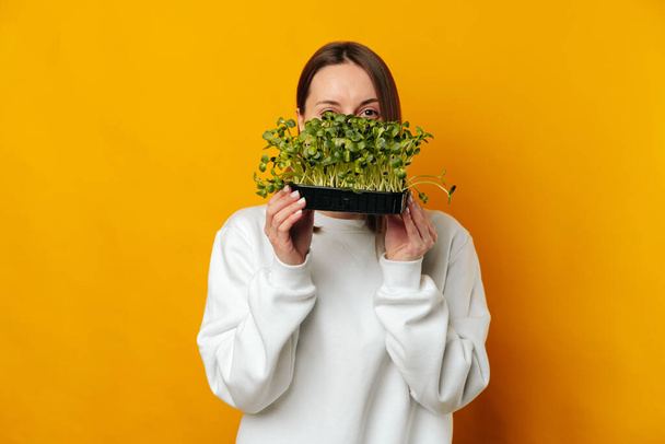 Eat micro greens and be healthy says a smiling woman hiding behind some over yellow background. - Fotoğraf, Görsel