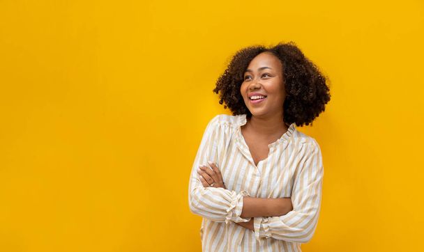 Retrato de estudio de una mujer afroamericana sonriendo en tela casual con una gran sonrisa y mano cruzada aislada sobre fondo amarillo para la confianza de la ama de casa y el estudiante - Foto, Imagen