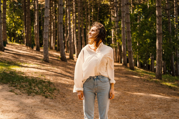 Giovane donna calma è in piedi tra gli alberi della foresta godendo il vento e la libertà in una giornata di sole. - Foto, immagini