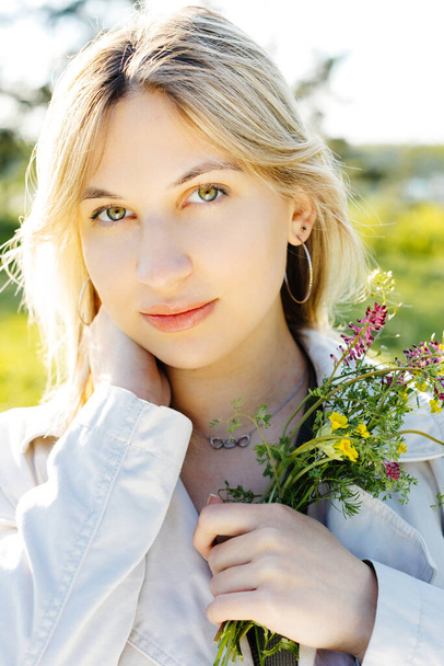 Spring lifestyle portrait of beautiful young woman smiling and holding bouquet of wild flowers. Happiness and love concept. - Photo, image