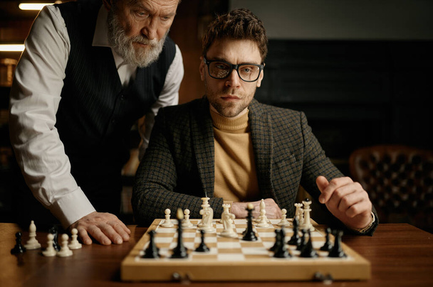 Senior homme enseignant aux jeunes hommes à jouer aux échecs expliquant les règles du jeu. Loisirs éducatifs - Photo, image