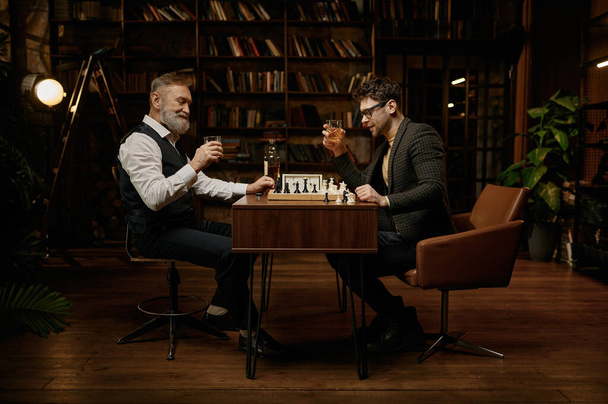 Elderly father and millennial son playing chess and drinking whisky while spending evening time together on weekend - Photo, Image
