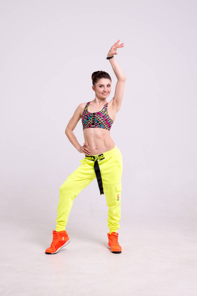 Attractive sporty woman wearing bright yellow pants jumping in the air against a white background. Dispersion and light flare effect on Womans body silhouette. - Zdjęcie, obraz