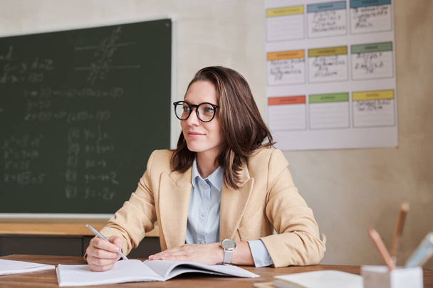 Warm-toned portrait of young female teacher sitting at desk in school classroom and smiling, copy space - Foto, immagini