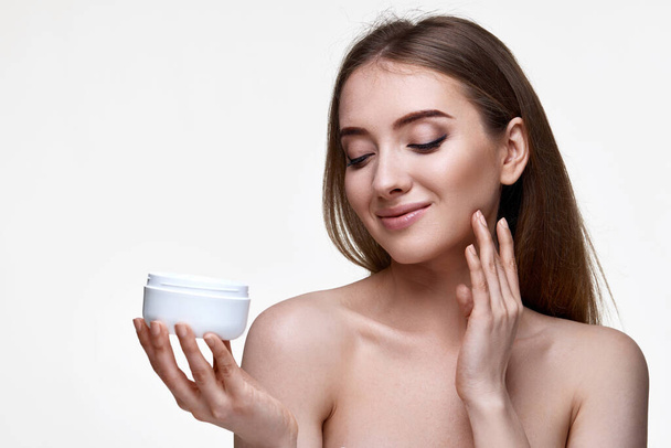 beautiful happy young woman applying skin care cream on her face on white background - Foto, Imagen