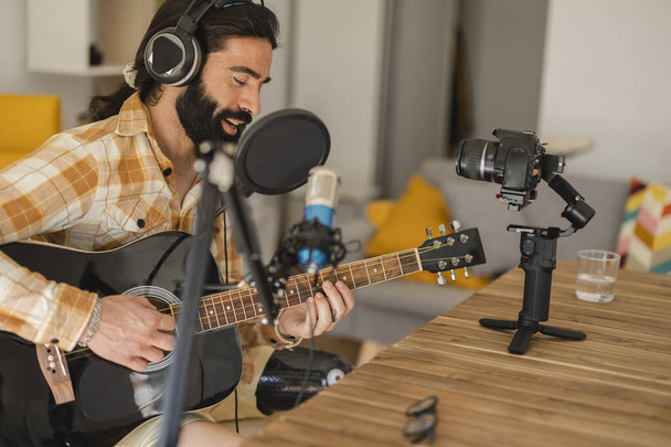 Homem hispânico executando música e cantando em microfone em estúdio de gravação de som em casa. O homem toca guitarra e canta uma canção. - Foto, Imagem