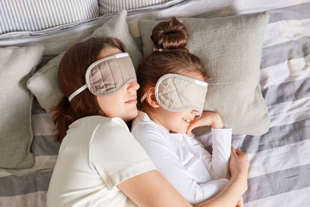 Little girl and her mother enjoying morning sleeping together hugging wearing blindfolds having day napping together in bedroom lazy weekend. - Fotó, kép