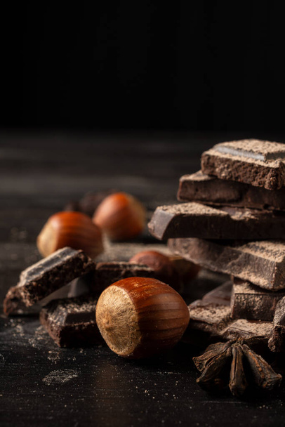 Close-up of hazelnuts with aniseed chocolate pieces, selective focus, on wooden table, black background, vertical, with copy space - Photo, Image