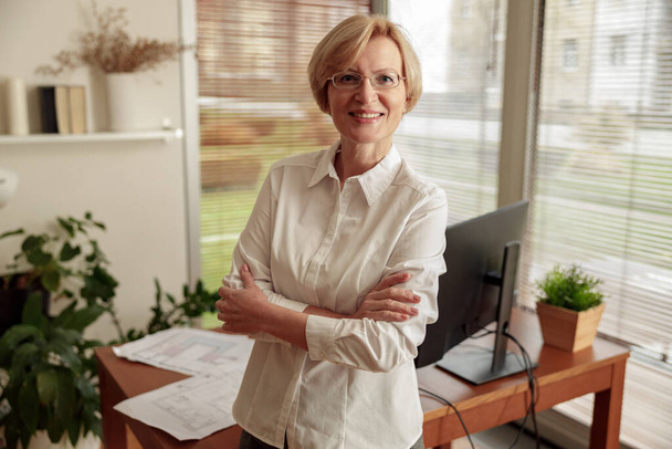 Smiling mature businesswoman in glasses standing on background of home office. High quality photo - Fotografie, Obrázek