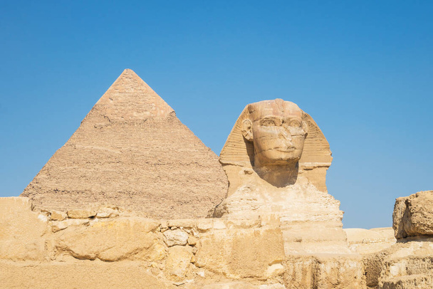Крупный план лица Великого Сфинкса с пирамидой на заднем плане в прекрасный день голубого неба в Гизе, Каир, Египет. копировальное пространство - Фото, изображение