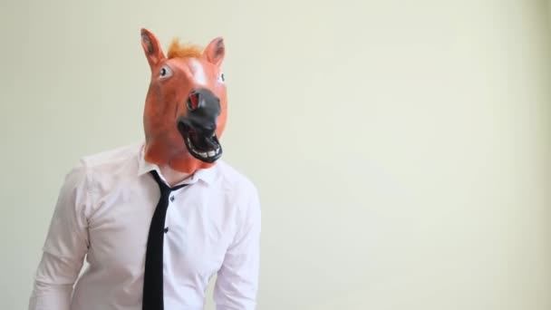 A strange man in a white shirt and a horse mask on a white background shows a thumb. Business horse. The concept of humor, fun. Office worker during party - Footage, Video