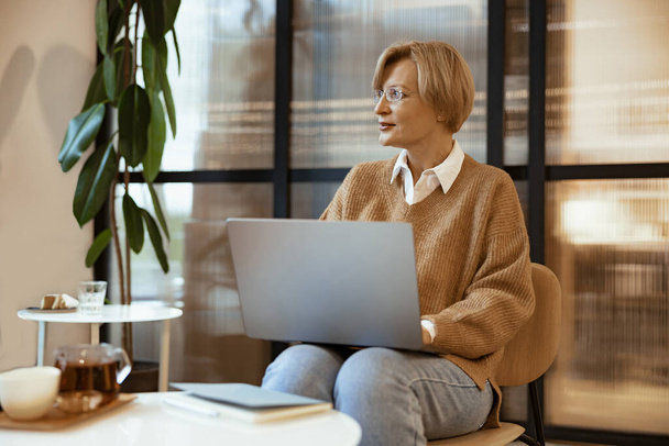 Middle aged business woman in casual clothes working laptop in coworking. Freelance work concept - Foto, Imagem