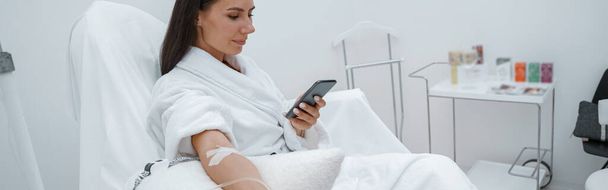 Woman in white bathrobe use phone during medical procedure in beauty clinic. High quality photo - Fotoğraf, Görsel