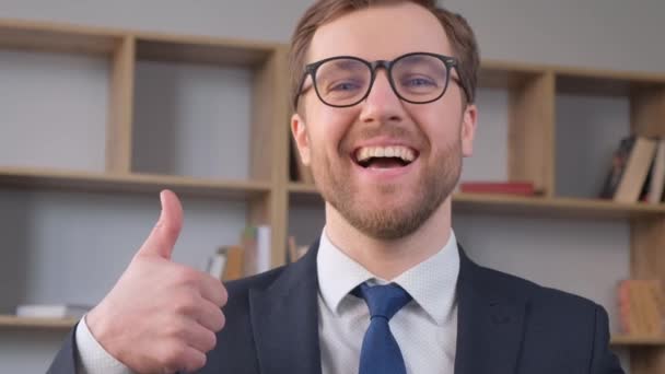 Nuori liikemies, joka näyttää peukalonsa yhdellä kädellä hymyillen seistessään keskellä toimistoa. Liikemiehen käsite - Materiaali, video