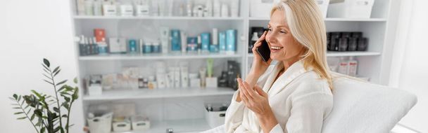 Beautiful Caucasian blonde mature woman in modern light cosmetology center talking on smartphone - Foto, immagini