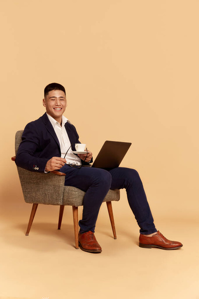 Remote work, online, sales, freelance. Portrait with smiling salesman, businessman holding laptop and working with pleasure over beige background. Concept of business, human emotions, mood, ad - Foto, Bild