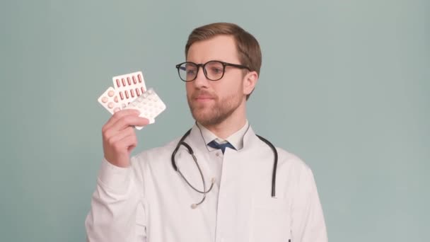 Een stijlvolle arts in bril toont pillen en raadt ze niet aan. Portret van een dokter op de achtergrond in de studio. 4k video - Video