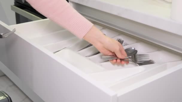 Una mano donna mette gli utensili da cucina in un cassetto. Scatola da cucina per forchette, cucchiai e coltelli. - Filmati, video