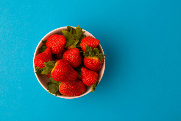 Fresh strawberries and green leaf in bowl isolated on blue background, top view - Foto, imagen