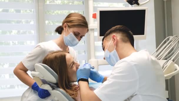 Een tandarts en een assistent onderzoeken de tanden van een vrouwelijke patiënt. Tandheelkundige behandeling in een moderne kliniek. 4k video - Video
