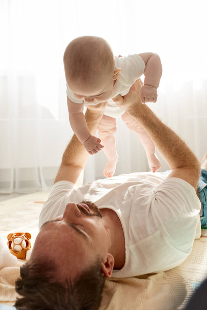 Happy dad segura seu bebê recém-nascido em seus braços enquanto deitado no chão em uma sala de crianças brilhantes. O pai olha para a criança com um olhar amoroso. Infância feliz e paternidade - Foto, Imagem