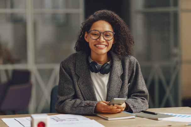 Woman freelancer smiling at camera while sitting with phone in modern coworking . High quality photo - Foto, Bild