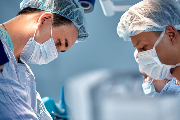 Karmaşık ve yoğun bir ameliyatta cerrahların yüzleri birbirine yakın, doktorlar hastaların hayatını ve cerrahların takım çalışmasını kurtarıyor. - Fotoğraf, Görsel