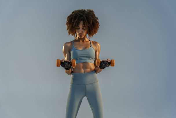 Muscular woman doing exercise with weight dumbbells on studio background  - Foto, Imagem