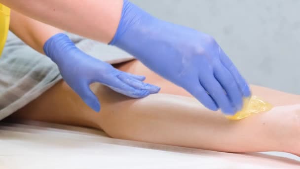 Primer plano de un esteticista depilando la pierna de un cliente. Depilación con pasta de azúcar. - Metraje, vídeo