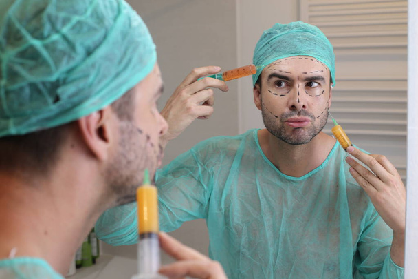retrato de joven guapo en traje de cirugía médica preparándose para la cirugía plástica delante del espejo - Foto, Imagen