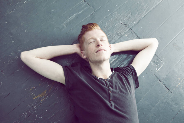 Relax, overhead and a man lying on the floor, hands behind head to sleep, rest or dream of peace. Quiet, sleeping and lifestyle with a young ginger male person relaxing on the ground from above. - Foto, Imagem
