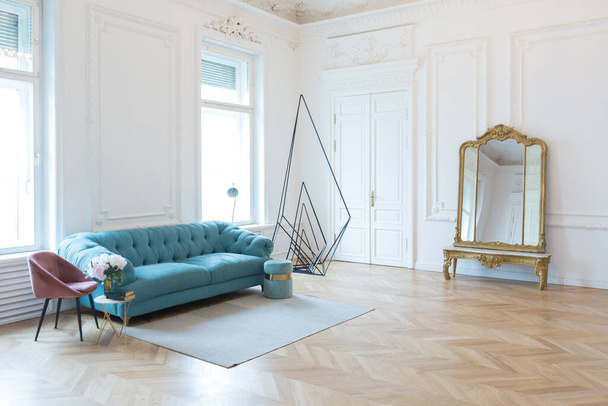 schicke geräumige helle Wohnung in einem alten Herrenhaus im klassischen Stil des 19. Jahrhunderts mit einer hohen Decke, die mit Stuckverzierungen an weißen Wänden und samtenen Möbeln mit goldenen Elementen dekoriert ist - Foto, Bild