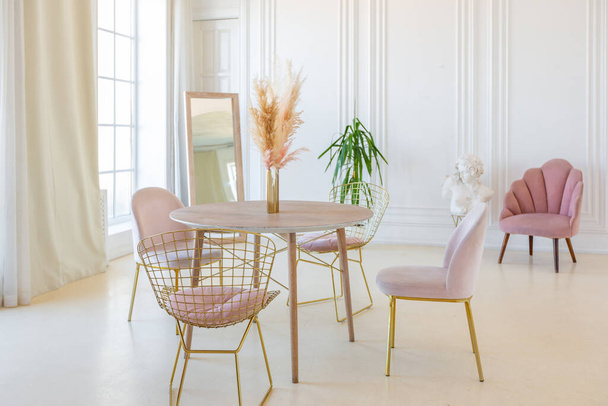 delicate and cozy light interior of the living room with modern stylish furniture of pastel pink color and white walls with stucco moldings in daylight - 写真・画像
