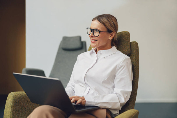 Empresária sentada na cadeira e trabalhando em laptop sobre fundo de co-trabalho. Foto de alta qualidade - Foto, Imagem