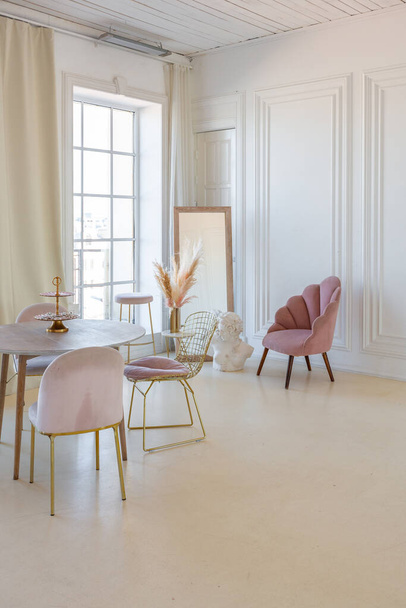 нежный и уютный светлый интерьер гостиной с современной стильной мебелью пастельно-розового цвета и белыми стенами с лепниной при дневном свете - Фото, изображение