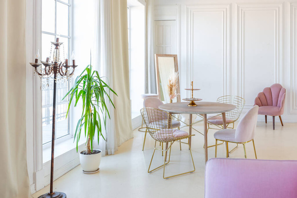 delicate and cozy light interior of the living room with modern stylish furniture of pastel pink color and white walls with stucco moldings in daylight - Fotó, kép
