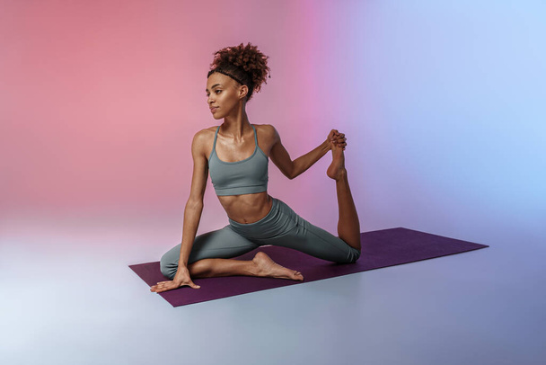 Athletic woman in sportswear doing stretching exercises on yoga mat on studio background  - Φωτογραφία, εικόνα