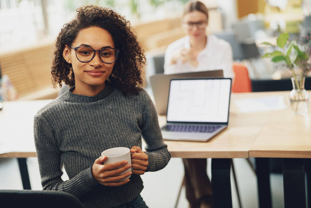 Woman freelancer drinking coffee in coworking on colleague background - Photo, image