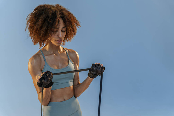 Silná žena ve sportovním oblečení provádí fitness cvičení s odbojovou kapelou na pozadí studia - Fotografie, Obrázek