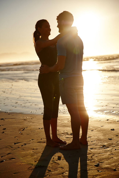 Moments to share and remember. a hugging couple silhouetted against a sunrise over the sea - Foto, Bild